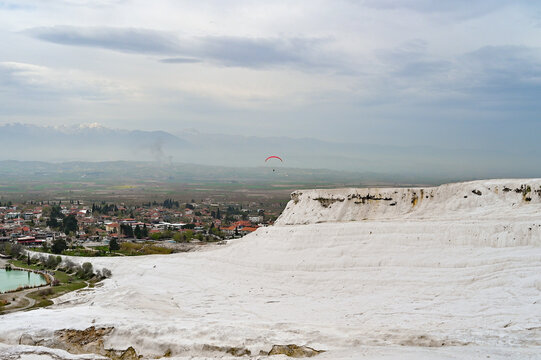 Red paraglider over the white travertine terraces of Pamukkale with a view of the valley, paragliding adventure, Denizli Province, Aegean Region, T&uuml;rkiye