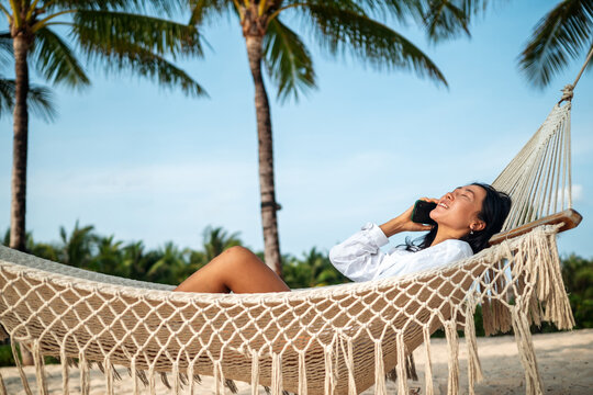 Cheerful woman talking on a smartphone during a sunny day at a tropical beach on summer vacation