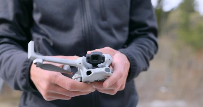 Close-up of hands unfolding propellers and arms of small compact drone outdoors