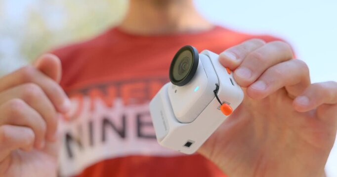 Close-up of hands attaching a magnetic accessory case to a compact action camera outdoors. Portable filming gear