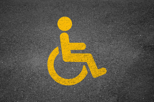 Yellow disabled parking symbol painted on asphalt. High angle view.
