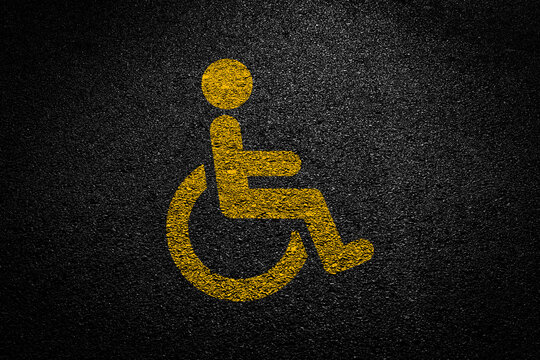 Yellow disabled parking symbol painted on asphalt. High angle view.