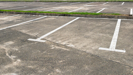 Obraz premium Empty parking lot on a clear day, asphalt ground with bright white parking lines, featuring a curb and green grass border, representing urban infrastructure and available space