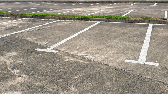Empty parking lot on a clear day, asphalt ground with bright white parking lines, featuring a curb and green grass border, representing urban infrastructure and available space