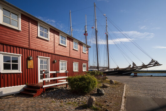Traditional sailing ship moored by a classic Falun red wooden house in Marstal harbor, Denmark