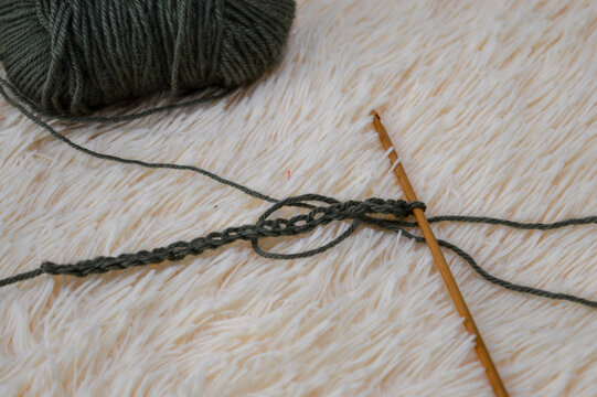 Wooden crochet hook inserted into a row of green wool yarn stitches resting on a white fluffy fur background close-up. Crocheting project, handmade yarn craft, needlework process, and cozy hobby conce