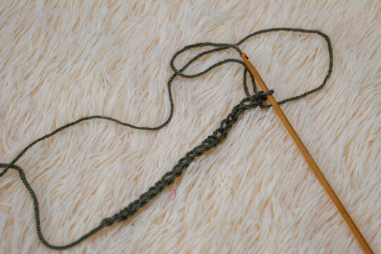 Wooden crochet hook inserted into a row of green wool yarn stitches resting on a white fluffy fur background close-up. Crocheting project, handmade yarn craft, needlework process, and cozy hobby conce