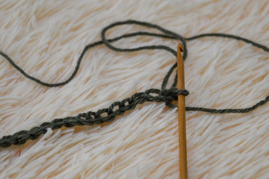 Wooden crochet hook inserted into a row of green wool yarn stitches resting on a white fluffy fur background close-up. Crocheting project, handmade yarn craft, needlework process, and cozy hobby conce