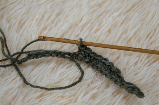 Wooden crochet hook inserted into a row of green wool yarn stitches resting on a white fluffy fur background close-up. Crocheting project, handmade yarn craft, needlework process, and cozy hobby conce