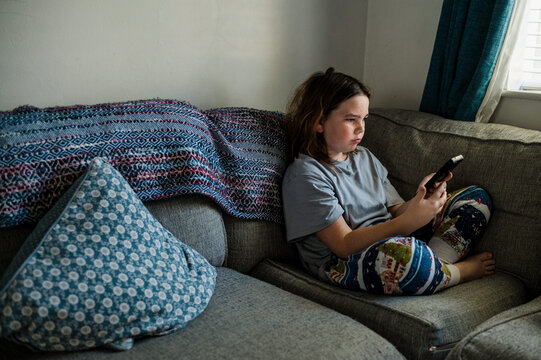 Child looks at mobile phone at home on couch