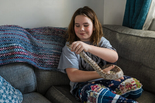 Child play with pet snake on the couch at home