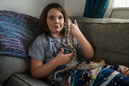 Child play with pet snake on the couch at home