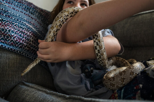 Child play with pet snake on the couch at home