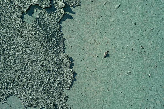 The weathered wall surface. Peeling teal paint flaking off a rough concrete wall revealing layers beneath. Ideal for grunge textures, decay concepts, deterioration backgrounds, and design overlays.