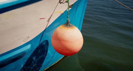 Orange buoy hanging from blue fishing boat hull © Banu