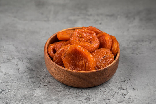 Sweet orange dried apricots kuraga in small round wooden bowl on gray textured stone background close up side view