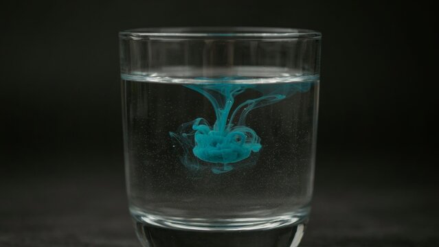 A clear glass filled with water showing blue ink spreading across the center.