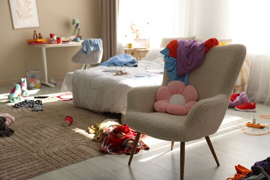 Scattered clothes on armchair and bed in messy teenager's room