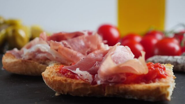 A close-up of a Spanish pan con tomate being prepared: a hand placing slices of Iberian jamon on toasted bread. Preparing a Spanish breakfast. High quality 4k footage