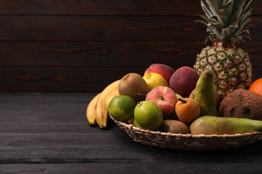 Different fresh fruits in wicker basket on black wooden table, closeup. Space for text