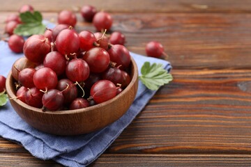 Fresh red gooseberries, green leaves and bowl on wooden table, closeup. Space for text © New Africa