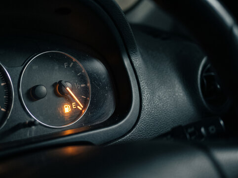 close up shot of car dashboard gauge cluster showing illuminated orange low fuel level warning light indicator icon with needle pointing to empty level during evening night drive