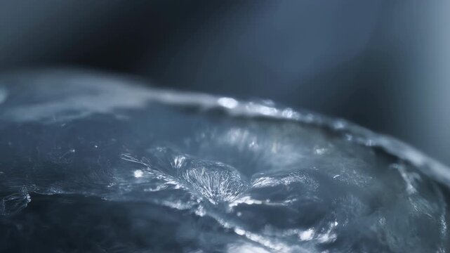Water surface with frozen ice texture glistens under cool light as subtle ripples move across transparent crystalline surface creating detailed winter atmosphere and natural reflective patterns
