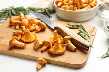 Wooden board with chanterelle mushrooms, knife, rosemary and spices on white table, closeup © New Africa