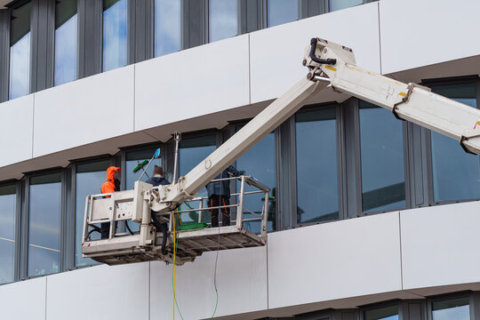 Workers in safety gear on a lift cleaning large glass windows of a modern office building