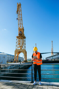 Dock worker using tablet next to crane in shipyard