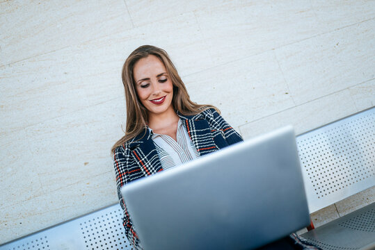 Businesswoman sitting on a bench, working on her laptop