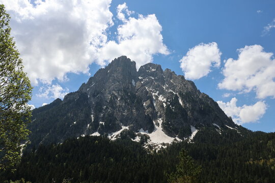 Vista majestuosa del pico Els Encantats con manchas de nieve bajo cielo nublado, Parque Nacional de Aig&uuml;estortes, Pirineos.
