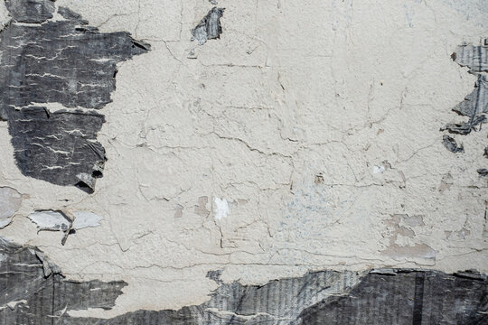 Textured wall with peeling posters and paint in shades of gray and beige