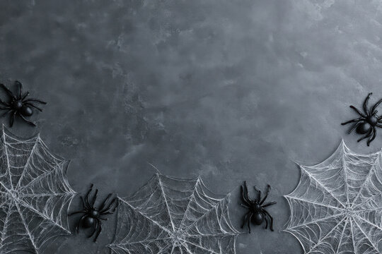 Halloween background with fake spider webs and plastic black spiders on dark grey textured surface, top view with copy space
