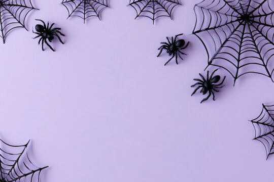 Flat lay halloween background with black plastic spiders and spider webs arranged on a pastel purple surface, festive holiday frame with copy space
