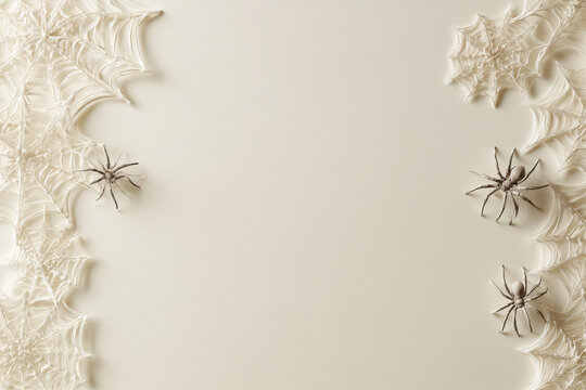 Minimalist halloween background with white spider webs and plastic spiders on offwhite paper with copy space