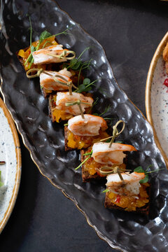 Sandwiches with shrimps and other dishes in plates on dark background. Delicious autumn dishes