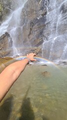 Obraz premium A person's hand reaching out to touch a small rainbow created by the mist of a beautiful waterfall in nature