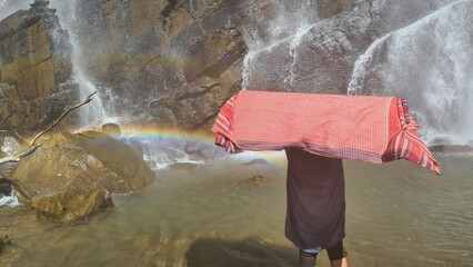 Obraz premium Person holding red cloth near majestic waterfall with rainbow and rocky cliffs in nature landscape