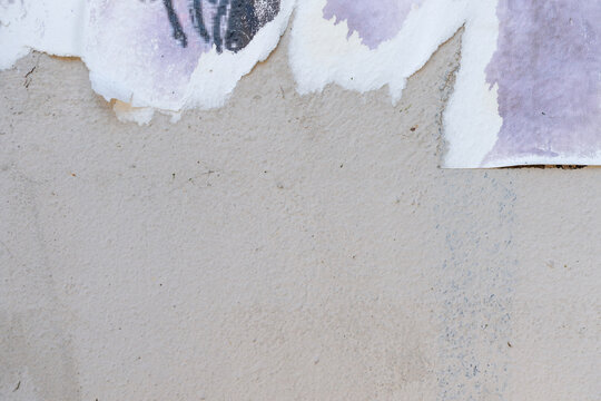 Close-up of textured gray wall with peeling old posters. Background surface shows mix of beige and purple colors, creating an urban aesthetic.