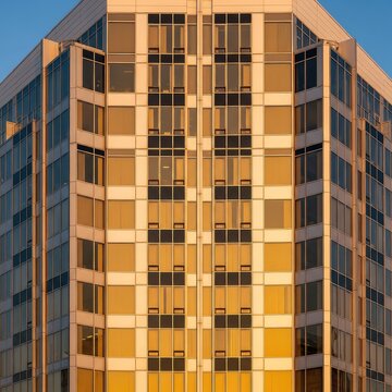 Modern architectural facade with symmetrical glass windows glowing in warm golden sunlight, showcasing corporate elegance and precision, financial, office, elegance