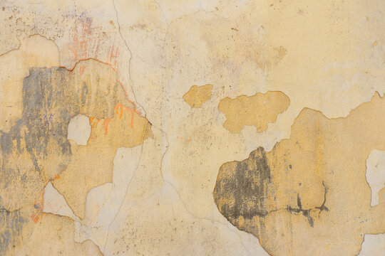 Textured wall with peeling paint in shades of yellow and beige. Old wall surface background shows signs of wear and age, creating an abstract pattern.