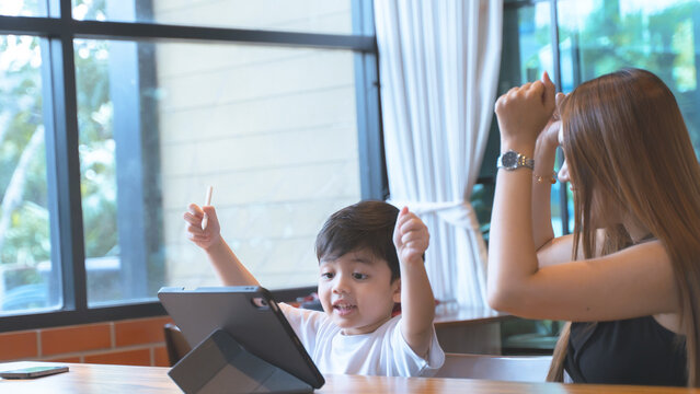 Happy young boy celebrating while using a tablet with his mother in a cafe