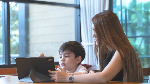 Mother and young son using a digital tablet together in a modern cafe
