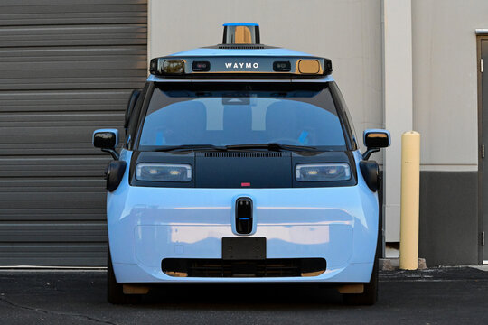 Waymo autonomous vehicle parked outside a facility, showing roof-mounted sensors and cameras used for driverless navigation, illustrating robotaxi technology and self-driving mobility
