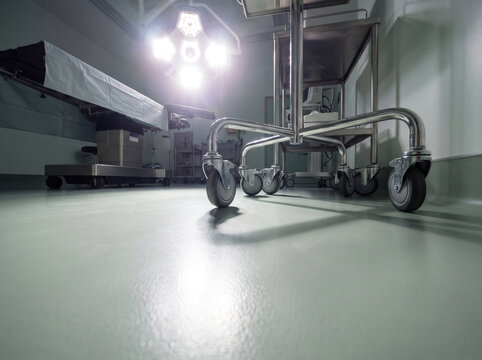 Low Angle View Across Seamless Operating Theatre Floor Toward Equipment Trolley Legs and Glowing Surgical Light Above
