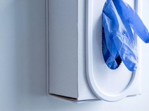 Close Up of Blue Nitrile Examination Gloves Emerging From Wall Mounted Dispenser Box in Clinical Setting