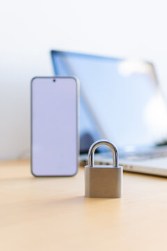 Vertical close up of padlock with smartphone and laptop in background