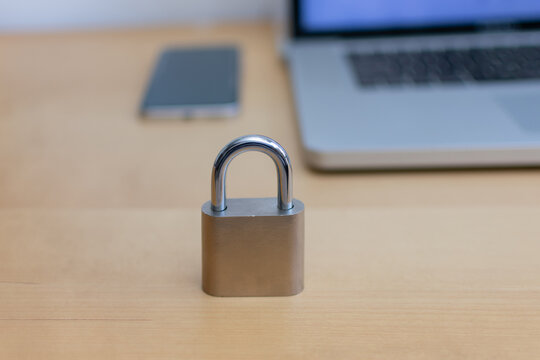 Front view of padlock with smartphone and laptop on wooden desk