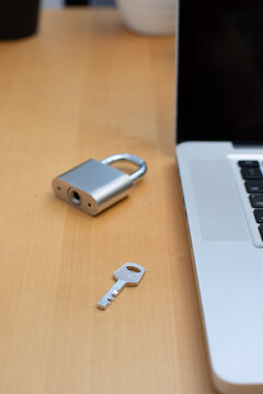 Vertical close up of padlock key with blurred lock and laptop